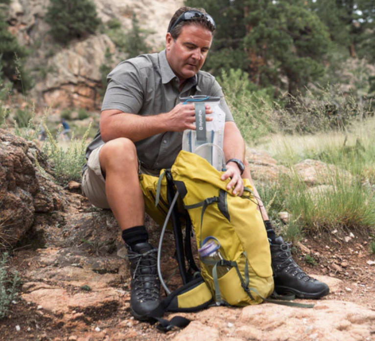 a man stashing his hydration reservoir in his backpack during a hike