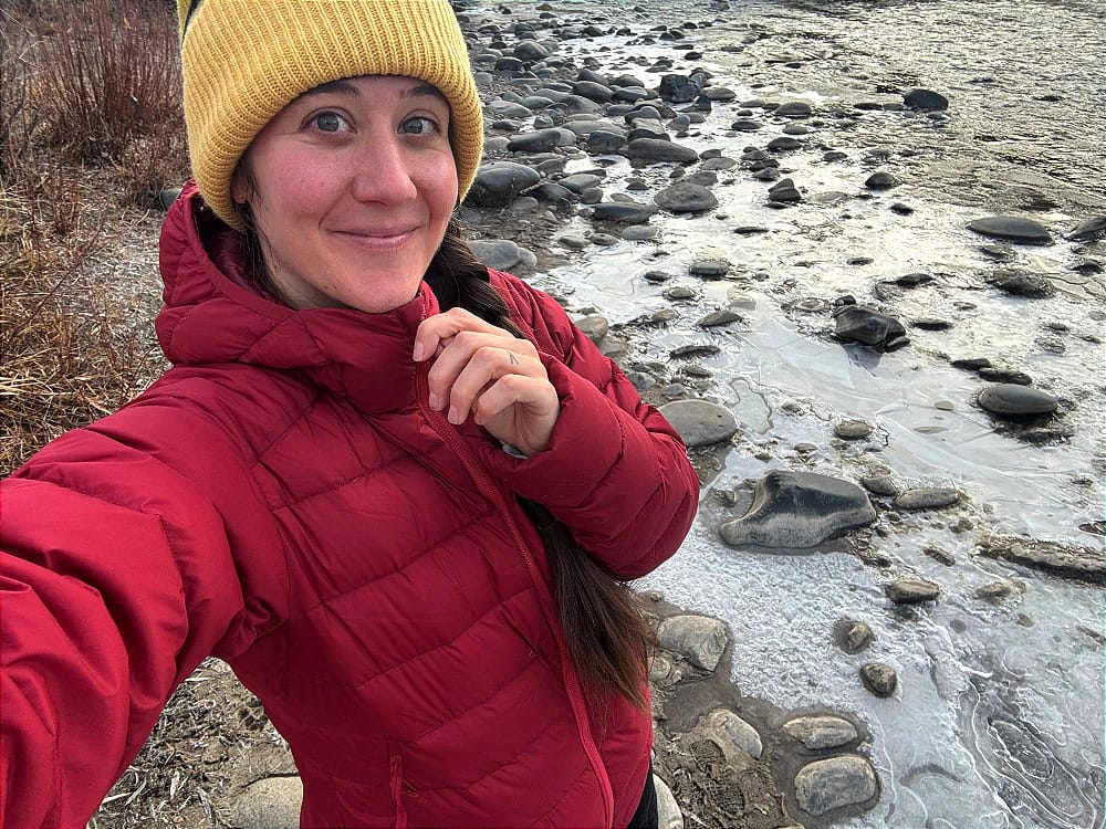 a woman take a selfie wearing the katabatic gear tincup down jacket in a freezing river scene in the southwest