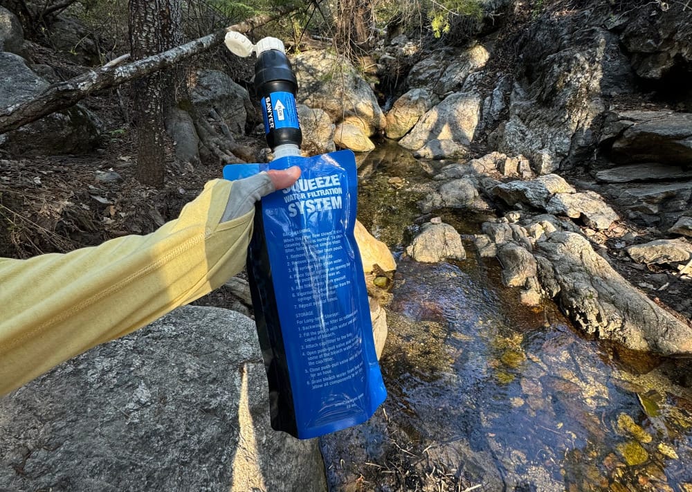 an ultralight backpacker uses a water filter to hydrate while hiking