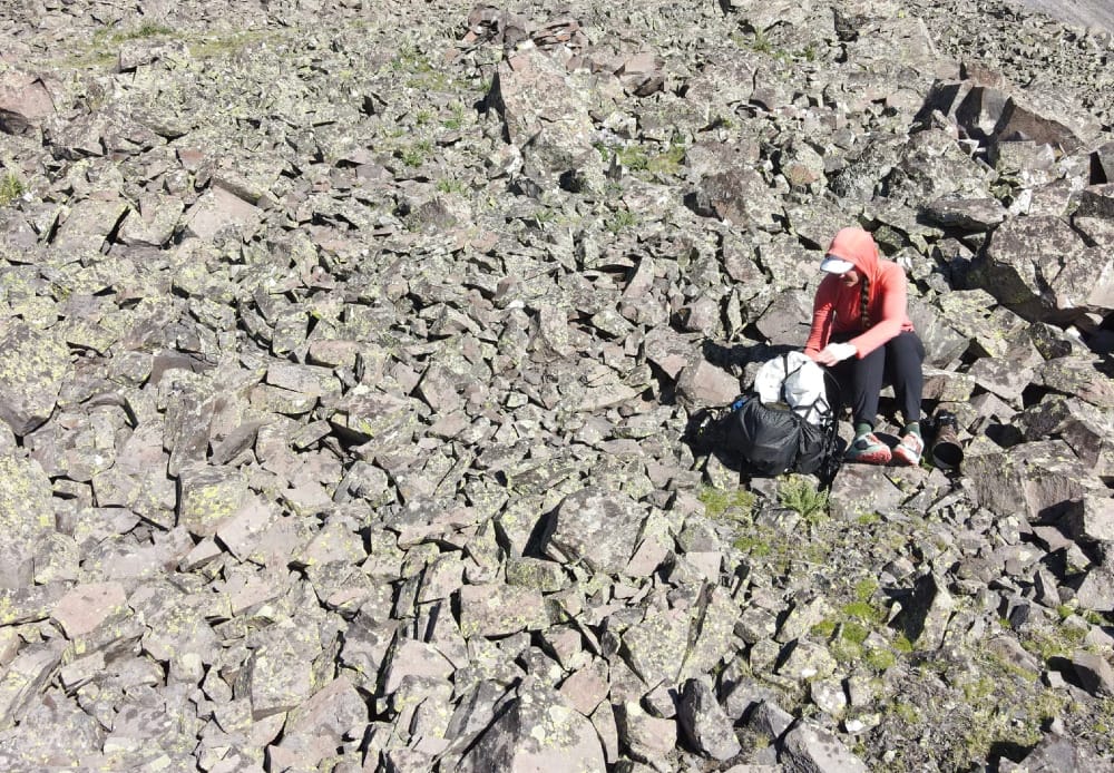 an ultralight backpacker sits on a mountain slope after a long day of hiking. she is taking off her backpack