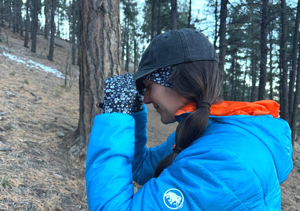 a hiker puts a hat on over her skida pursuit headband. she is also wearing skida liner gloves because it's a very cold winter day.