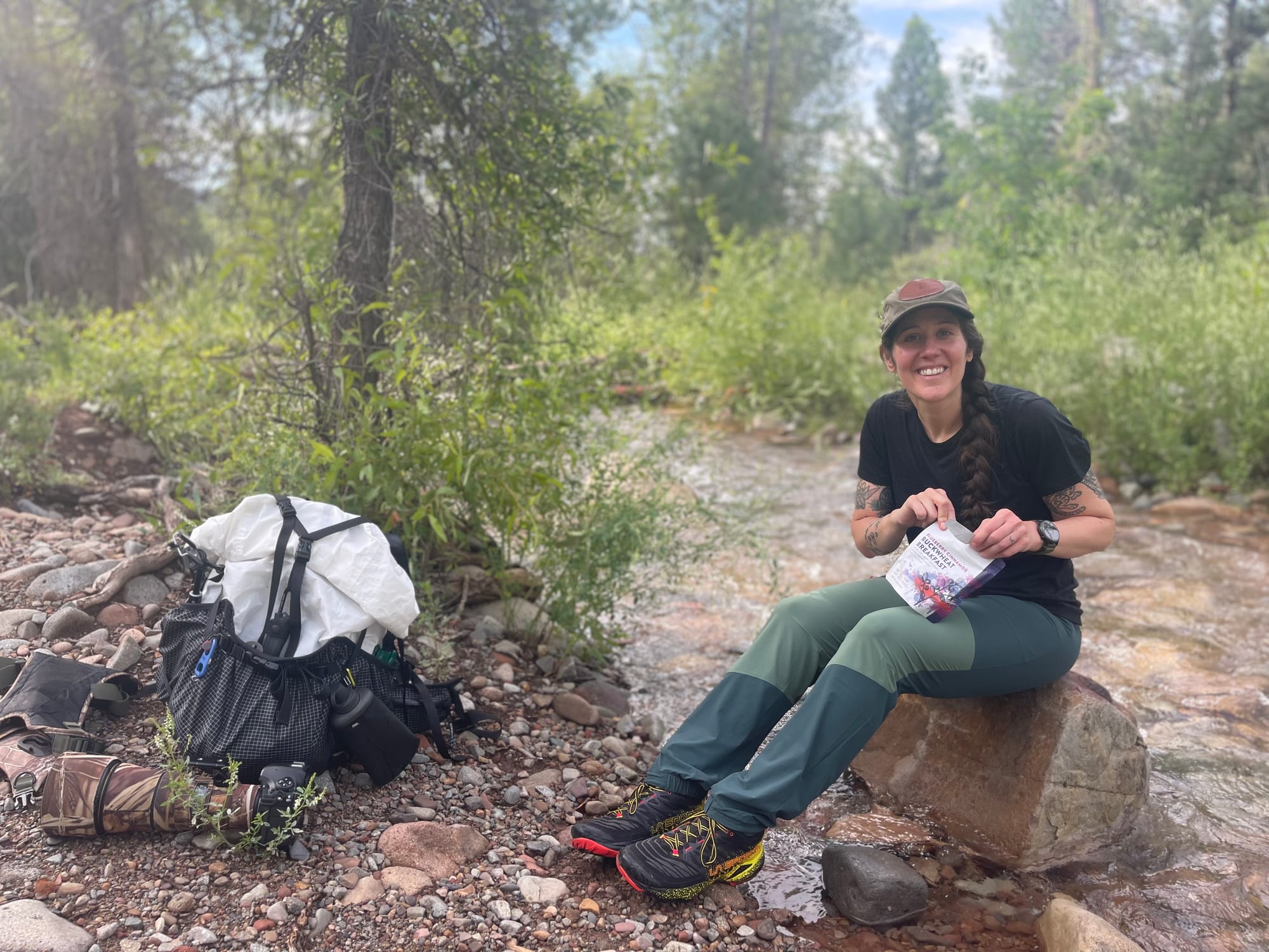 a hiker stops to have lunch along a mountain creek with a hyperlite mountain gear backpack next to her