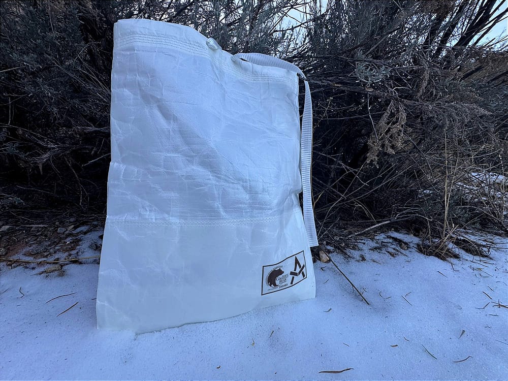 The Grizzly Bear Resistant Ultralight Food Locker By Adotec Gear sitting in snow near a bush as campers pulled it down to retrieve breakfast 