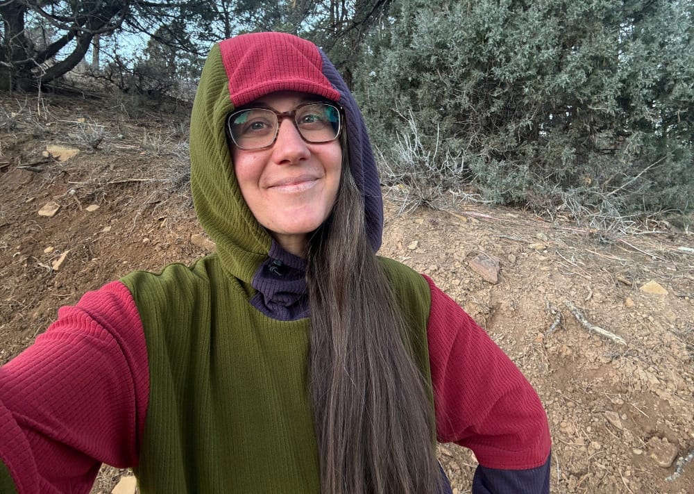 a woman take s selfie wearing one of the best fleece hiking hoodies of the year by sambob in a juniper forest of the southwest