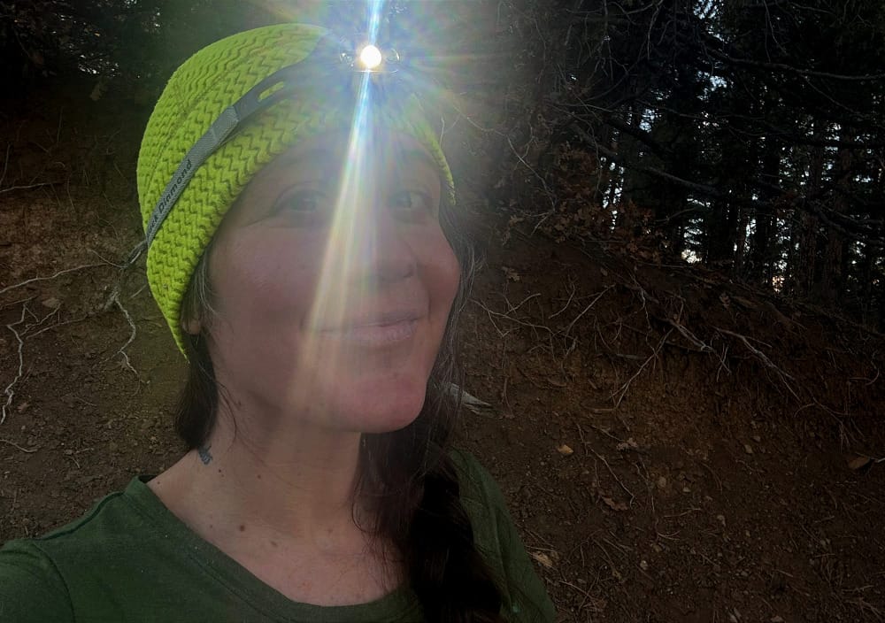 a woman wearing the deploy headlamp by black diamond outside in the southwest demonstrating the headlamps bright light and compact size