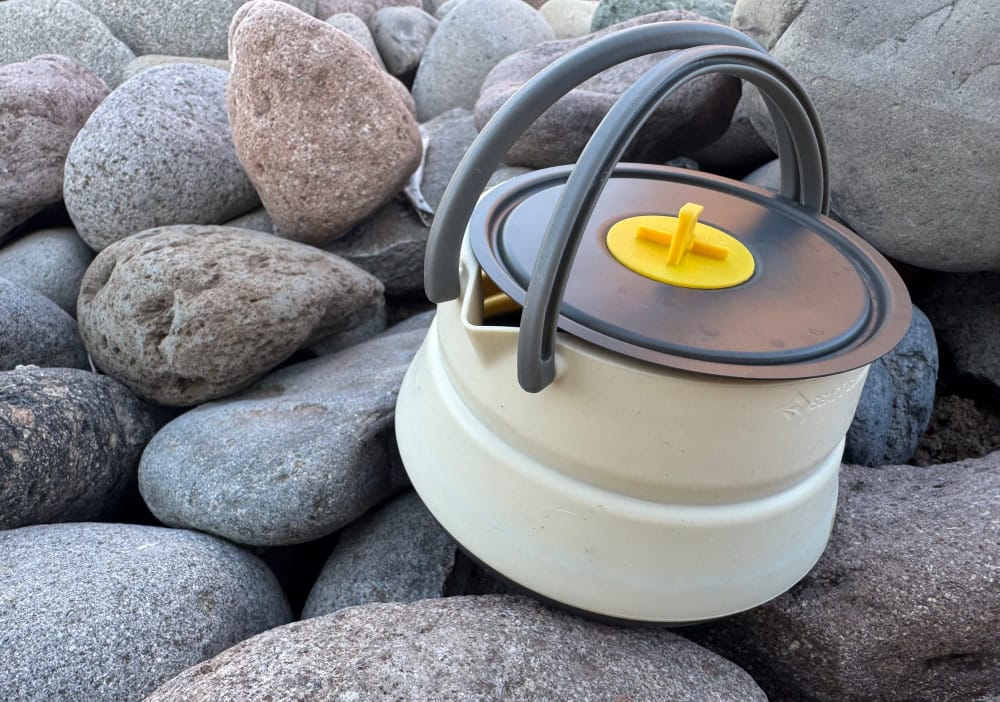 the Frontier Ultralight Collapsible Kettle By Sea To Summit sitting on some river rocks in the mountains