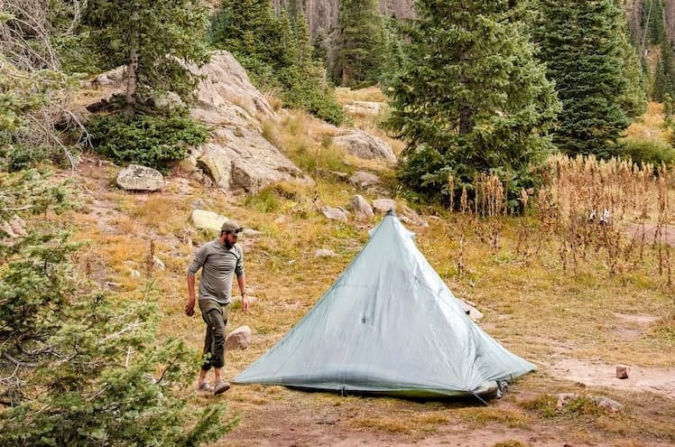 a backcountry hiker pitches his hyperlite mountain gear tent in a high mountain forest