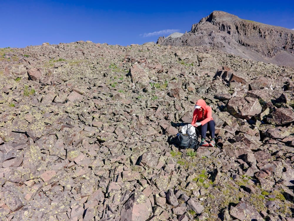 a backpacker sits on a high alpine talus field with a hyperlite mountain gear backpack holding all of their gear