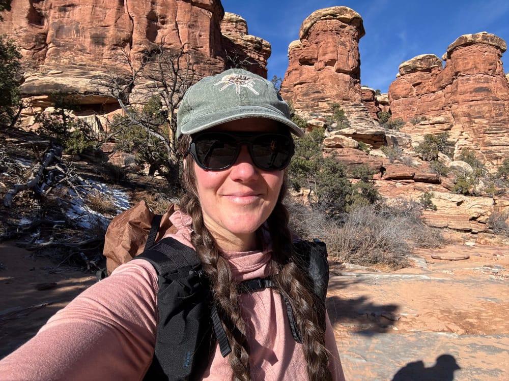 a woman wears Teton Sunglasses By Ombraz during a hike in a beautiful, rugged canyon.