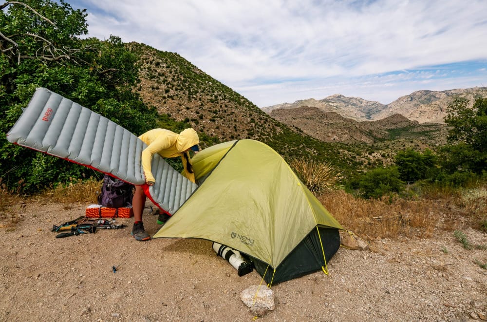 an ultralight backpackers inflates her airpad on a mountain ridge and puts it into her ultralight tent