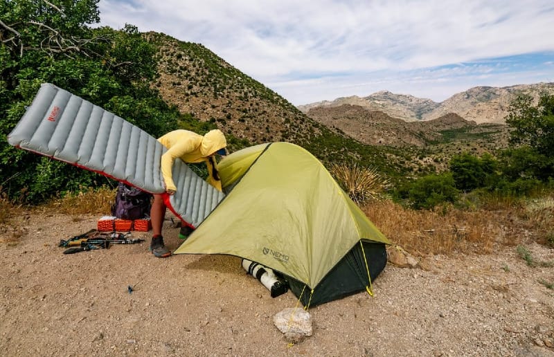 a backpacker pitching the Hornet OSMO Ultralight Backpacking Tent By NEMO Equipment against a backdrop of beautiful mountains