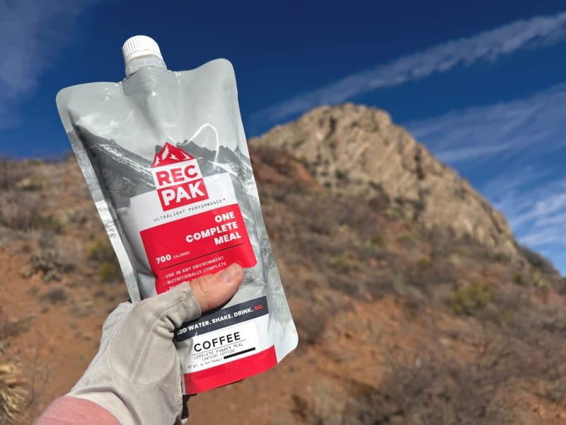 Recpak One Complete Meal being held out against a mountain during a backpacking trip