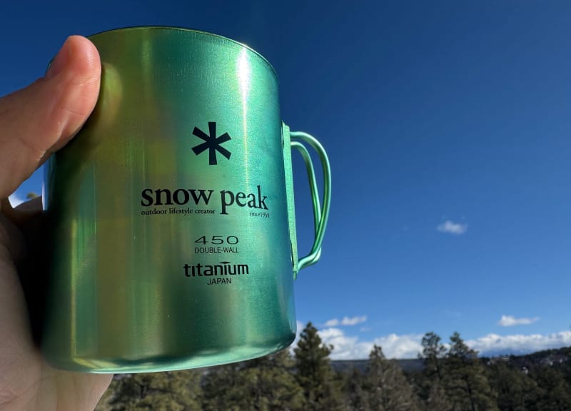 a hiker holds the Ti-Double 450 Anodized Mug By Snow Peak on a sunny day in the woods