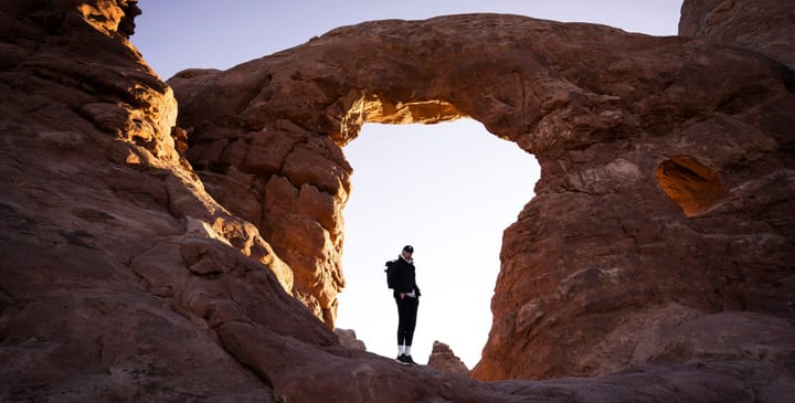 a hiker standing under an arch in the desert southwest