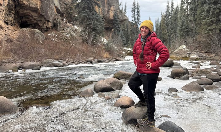 a woman wearing the katabatic gear tincup down jacket along a river on a cold winter morning