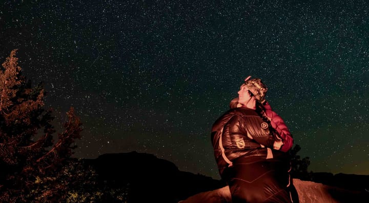 a winter backpacker sits outside in her nemo equipment sonic -20° down ultralight sleeping bag under a sea of stars