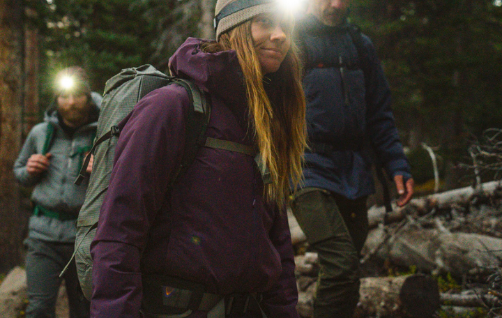 the paka apu parka is worn by a woman backpacking on a very cold winter day with a headlamp on and with friends