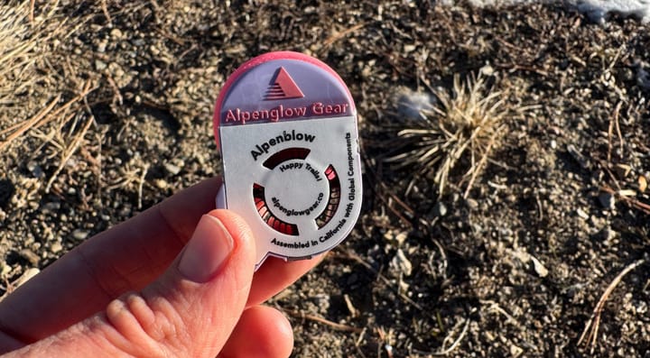 A hand holding the Alpenblow Micro Inflator By Alpenglow Gear outside on an adventure as the sun goes down