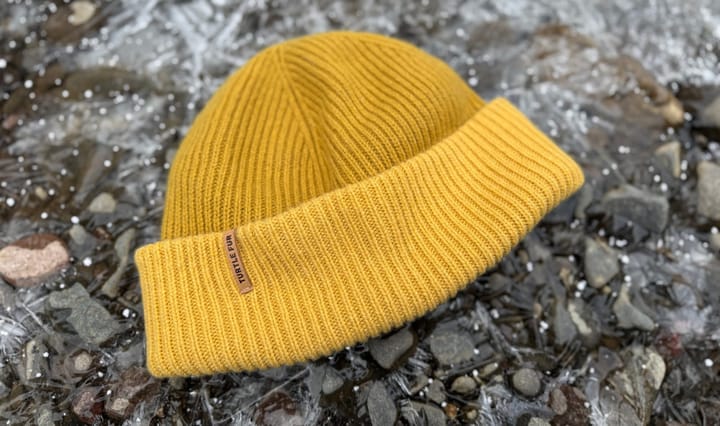 the whitman beanie from turtle fur is laying on snow and ice and it is yellow made of yak and merino wool