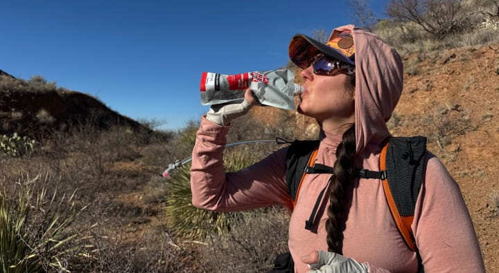 a woman drinks a Recpak One Complete Meal while out on a big backpacking adventure in the southwest